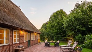 A thatched-roof building with a brick facade, a paved patio with outdoor furniture, and a well-maintained lawn. - FH Luhe-Hof - Historisches Reetdachanwesen (Winsen (Luhe))