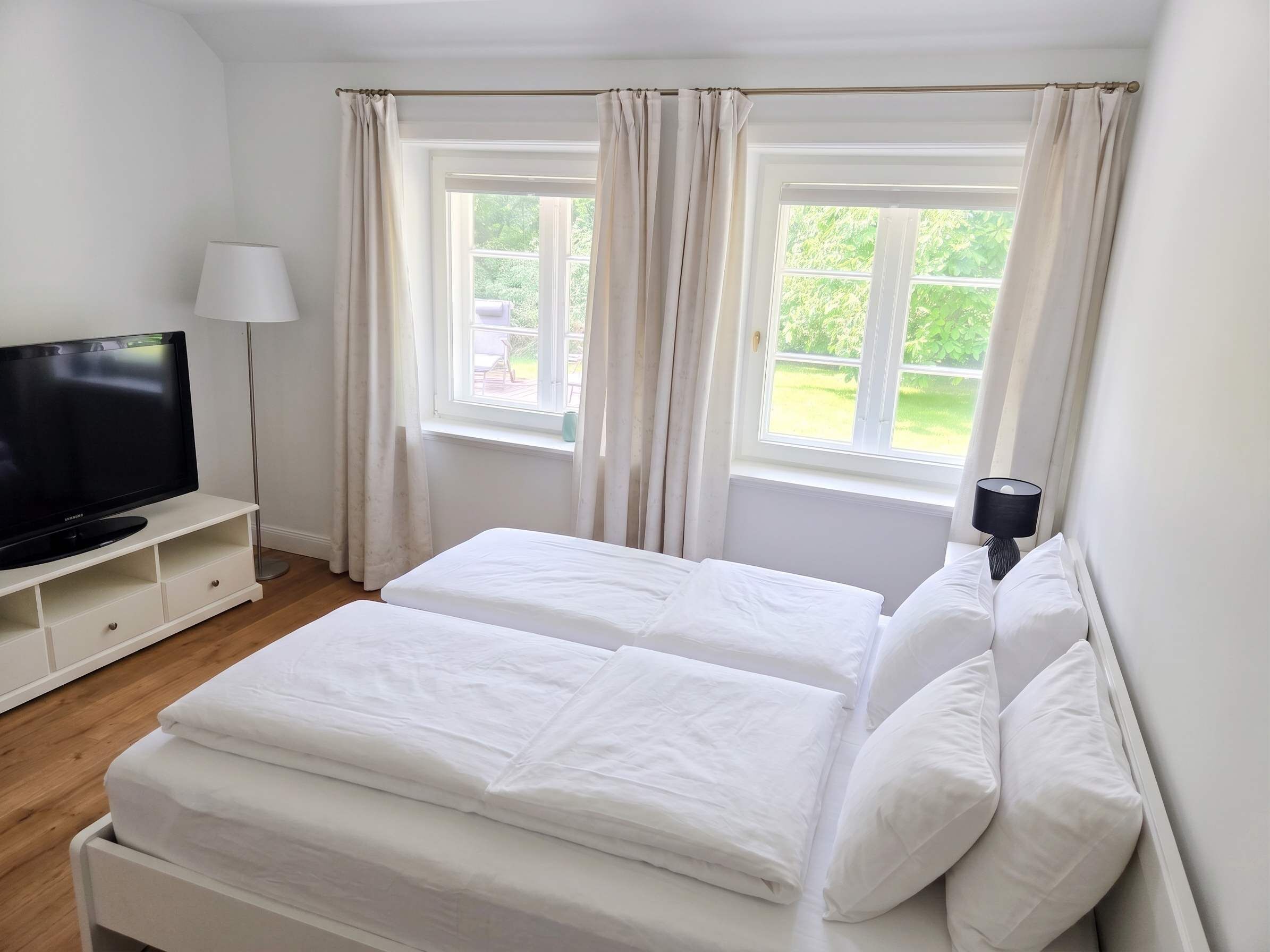 Quarto com duas camas, televisão, luminária e janelas com cortinas.