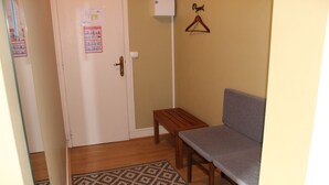 A small room with a wooden bench, a grey sofa, a patterned rug, and a door with a poster. - La Halte Solognote (Brinon-sur-Sauldre)