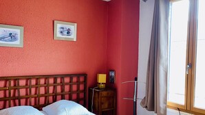 A room with a bed, a bedside table, a lamp, a window with curtains, and artwork on the wall. - La Halte Solognote (Brinon-sur-Sauldre)