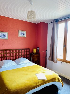 A room with a bed, a bedside table, a lamp, a window with curtains, and artwork on the wall. - La Halte Solognote (Brinon-sur-Sauldre)