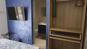 A bedroom with a bed, a TV, a wooden wardrobe, and a bathroom visible through an open door. - Room with all the amenities (Termini Imerese)
