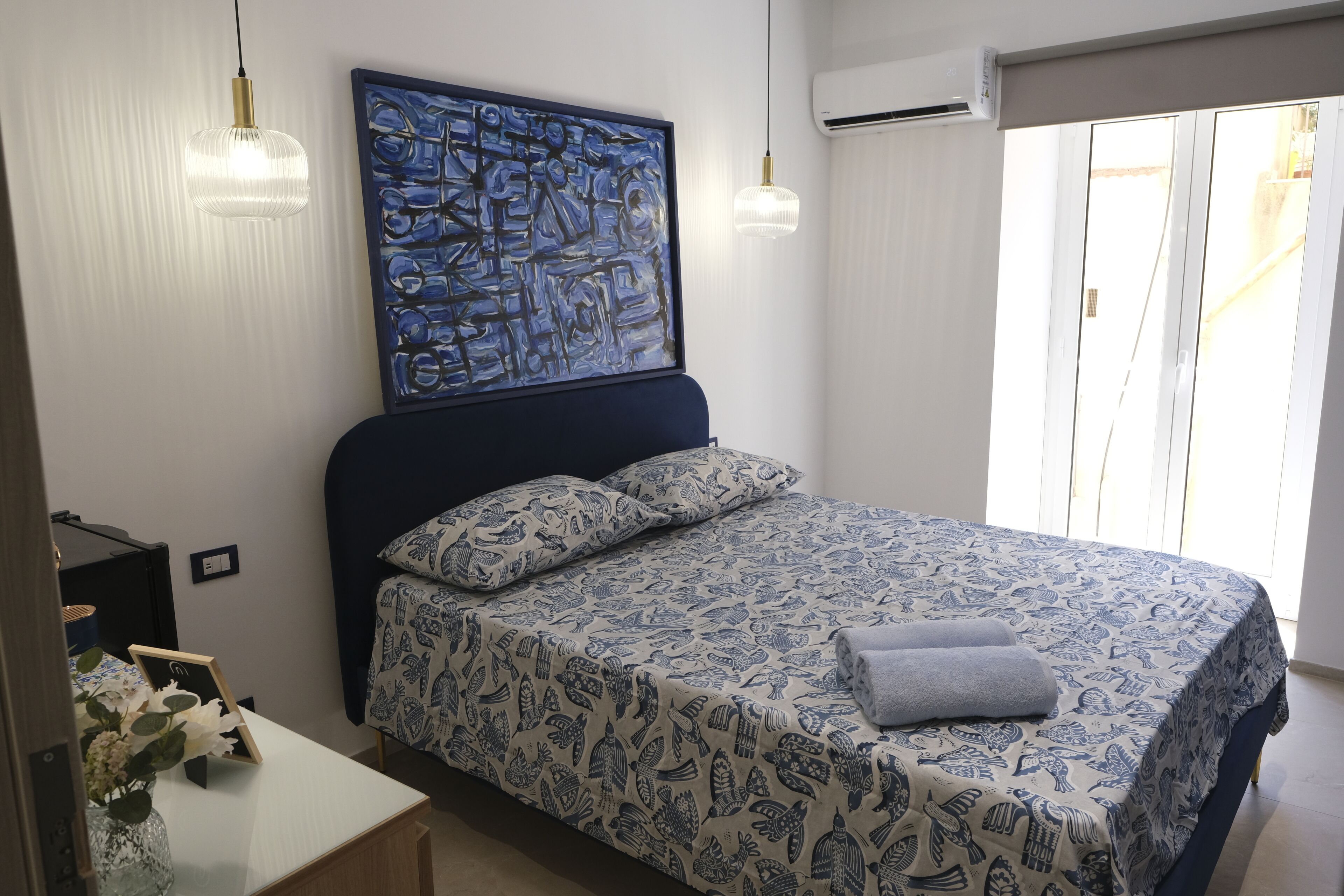 Una camera da letto con un letto, un quadro, un comodino, una lampada e un condizionatore d'aria.