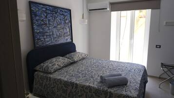 A bedroom with a bed, a painting, an air conditioning unit, and a window with curtains.
