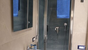 A modern bathroom with a glass-enclosed shower, a white sink, and a dark vanity. - Room with all the amenities (Termini Imerese)