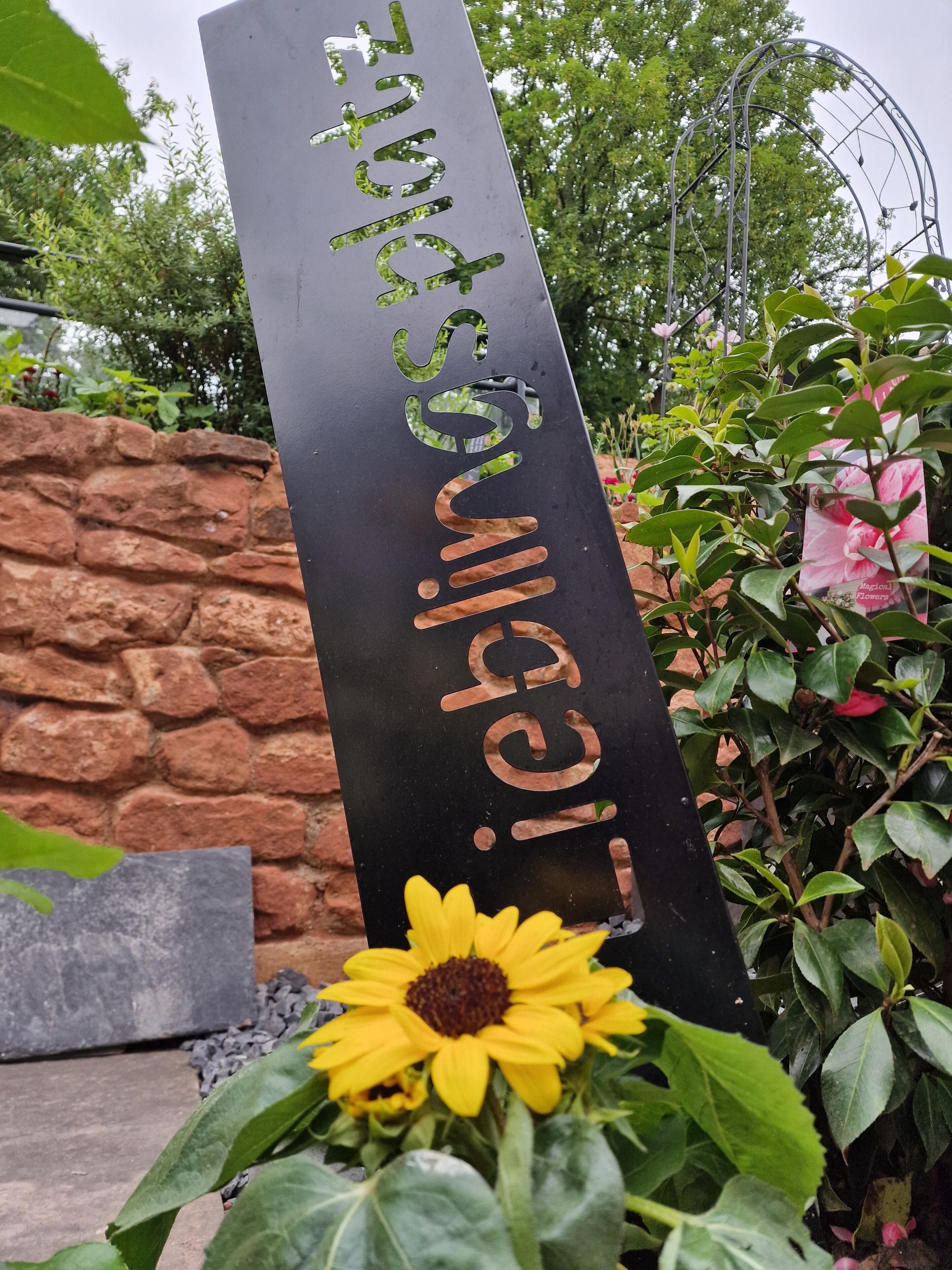 Ein vertikales Schild mit arabischer Schrift, eine Steinsäule und eine Sonnenblume.