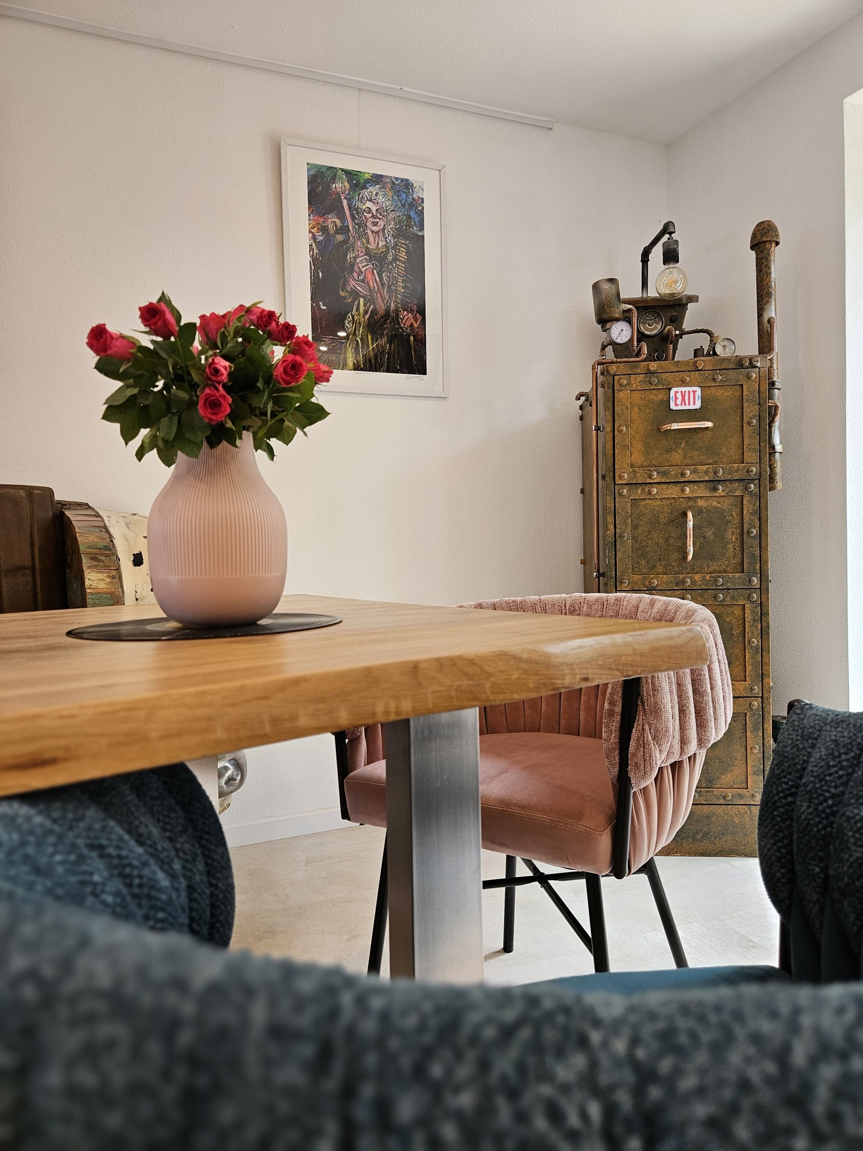 Ein Essbereich mit Holztisch, Blumen in einer Vase, einem Küstenmöbelkorpus und einem gerahmten Bild an der Wand.