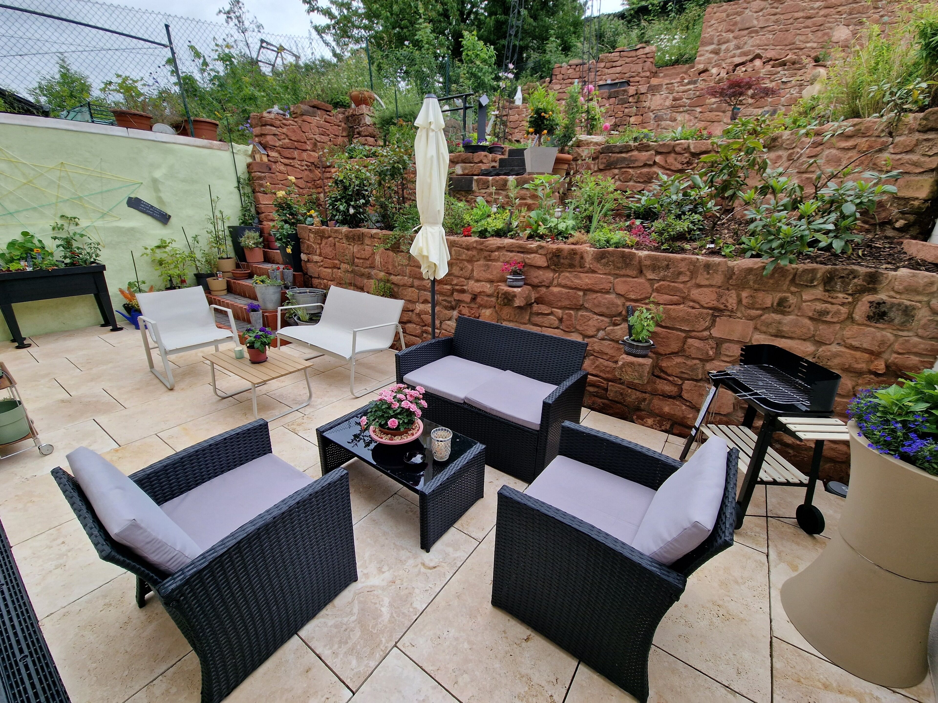 Eine Terrassenfläche mit Korbmöbeln, einem Tisch mit Topfpflanze und einer Steinmauer mit Kletterpflanzen.