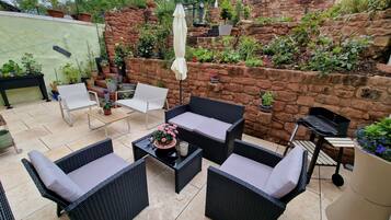 Eine Terrassenfläche mit Korbmöbeln, einem Tisch mit Topfpflanze und einer Steinmauer mit Kletterpflanzen.