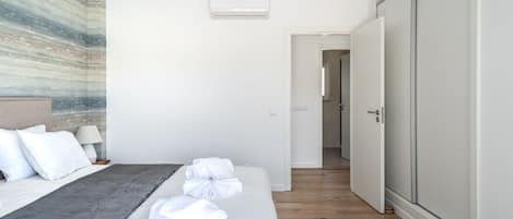 Habitación de hotel con cama, mesita de noche con lámpara, aire acondicionado de pared y armario.