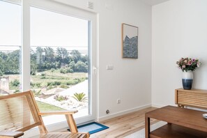A room with a sliding glass door leading to a garden, a wooden bench, a dining table, and a framed artwork on the wall. - Mosteiros Escape with Pool & BBQ by Lisbeyond (Mosteiros)