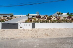 A modern building with a white exterior, a paved entrance, and a landscaped garden with various plants. - Mosteiros Escape with Pool & BBQ by Lisbeyond (Mosteiros)