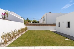 A modern residential property with a well-maintained lawn, white walls, and a wooden fence. - Mosteiros Escape with Pool & BBQ by Lisbeyond (Mosteiros)
