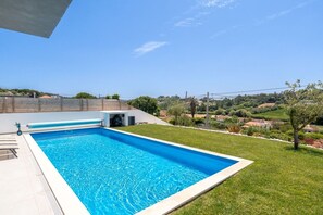 A rectangular swimming pool with a clear blue water surface, surrounded by a white deck and a grassy area. - Mosteiros Escape with Pool & BBQ by Lisbeyond (Mosteiros)