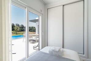 A bedroom with a bed, a window, and a view of an outdoor swimming pool. - Mosteiros Escape with Pool & BBQ by Lisbeyond (Mosteiros)