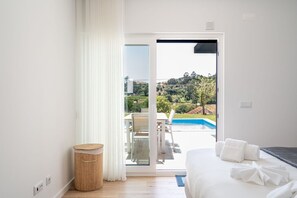 A bedroom with a bed, a small round table, and a view of a swimming pool and greenery outside. - Mosteiros Escape with Pool & BBQ by Lisbeyond (Mosteiros)