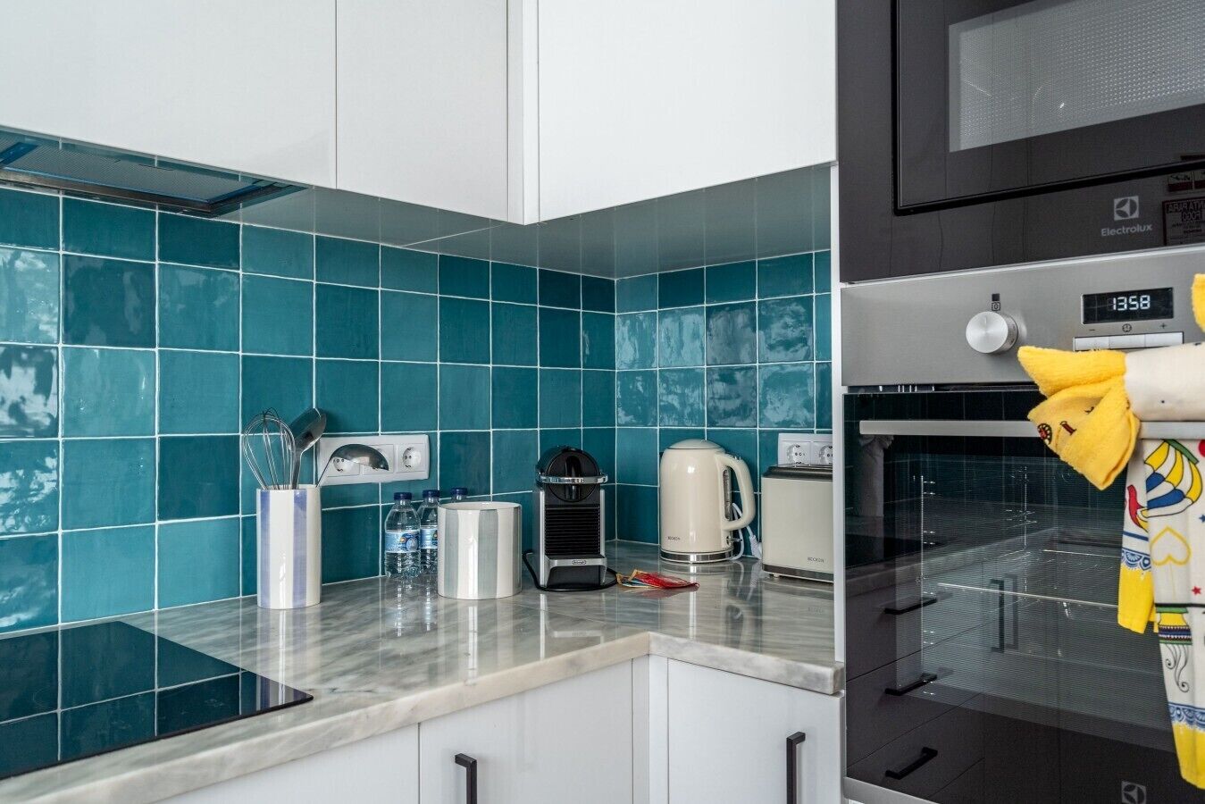 Een keuken met blauwgroene tegels, een koffiezetapparaat, een broodrooster en een magnetron.
