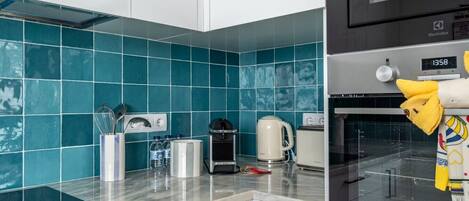 Een keuken met blauwgroene tegels, een koffiezetapparaat, een broodrooster en een magnetron.