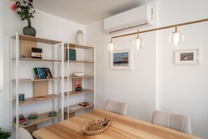 A dining area with a wooden table, chairs, a bookshelf, and wall-mounted lights. - Mosteiros Escape with Pool & BBQ by Lisbeyond (Mosteiros)