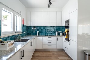 A modern kitchen with white cabinets, teal backsplash, and wooden flooring. - Mosteiros Escape with Pool & BBQ by Lisbeyond (Mosteiros)