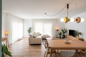Ein modernes Wohnzimmer mit einer Couch, einem Esstisch und Stühlen. Ein Fernseher steht auf einer Holzkommode.