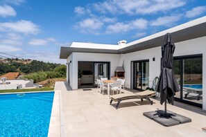 A modern house with a swimming pool, outdoor seating, and a large sliding glass door. - Poolside Retreat in Mosteiros by Lisbeyond (Vidais)