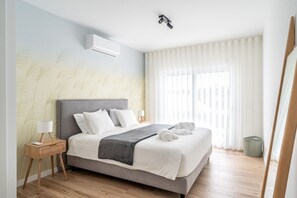 Ein modernes Hotelzimmer mit einem Bett, Nachttischen, einer Lampe und einem großen Fenster mit Vorhängen.