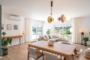 Ein modernes Wohnzimmer mit Essbereich, großen Fenstern und Blick auf einen Pool.
