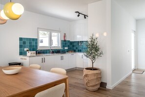 A modern kitchen with white cabinets, teal backsplash, and a dining area with a wooden table and chairs. - Poolside Retreat in Mosteiros by Lisbeyond (Vidais)
