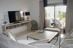 A living room with a flat-screen TV, a sofa, a coffee table, and a wicker chair. - Garden Apartment. Golf by the Sea in Estepona (Estepona)