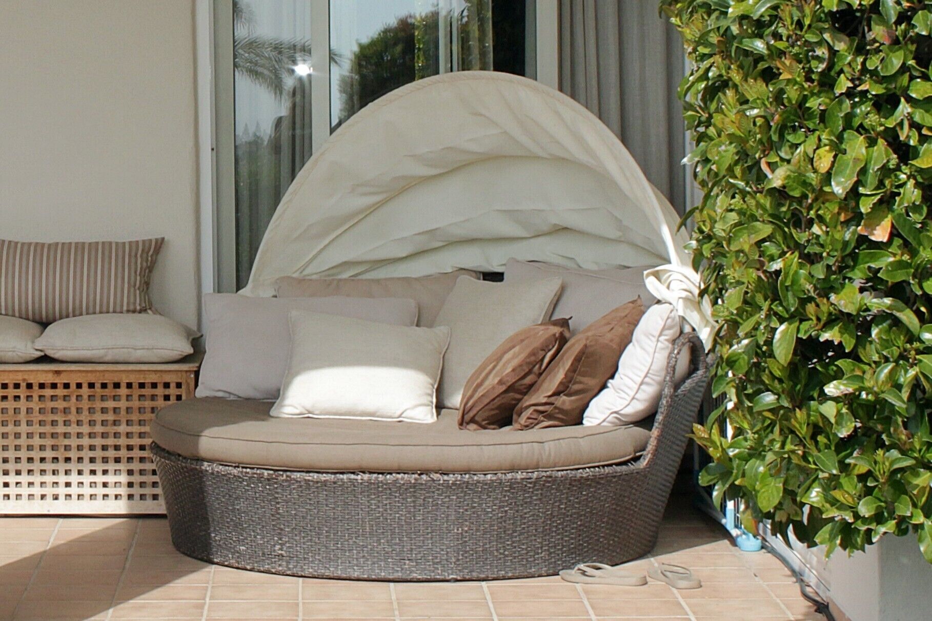 Un espace de détente extérieur aménagé avec des meubles en osier, des coussins, un panier tressé et une plante en pot.