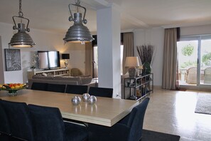 A dining area with a table, chairs, and a fruit bowl. There is a sofa and a television in the background. - Garden Apartment. Golf by the Sea in Estepona (Estepona)
