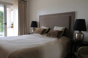 A hotel room with a large bed, two bedside lamps, and a view through a window with curtains. - Garden Apartment. Golf by the Sea in Estepona (Estepona)