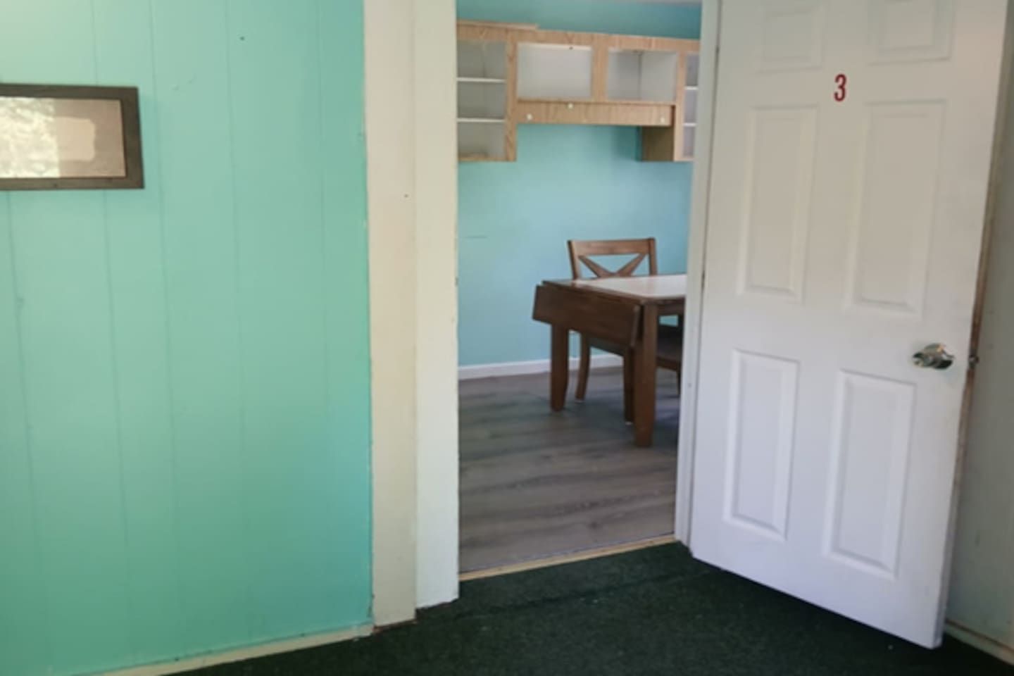 Un pasillo con una puerta marcada '3', una silla de madera y un estante al fondo.