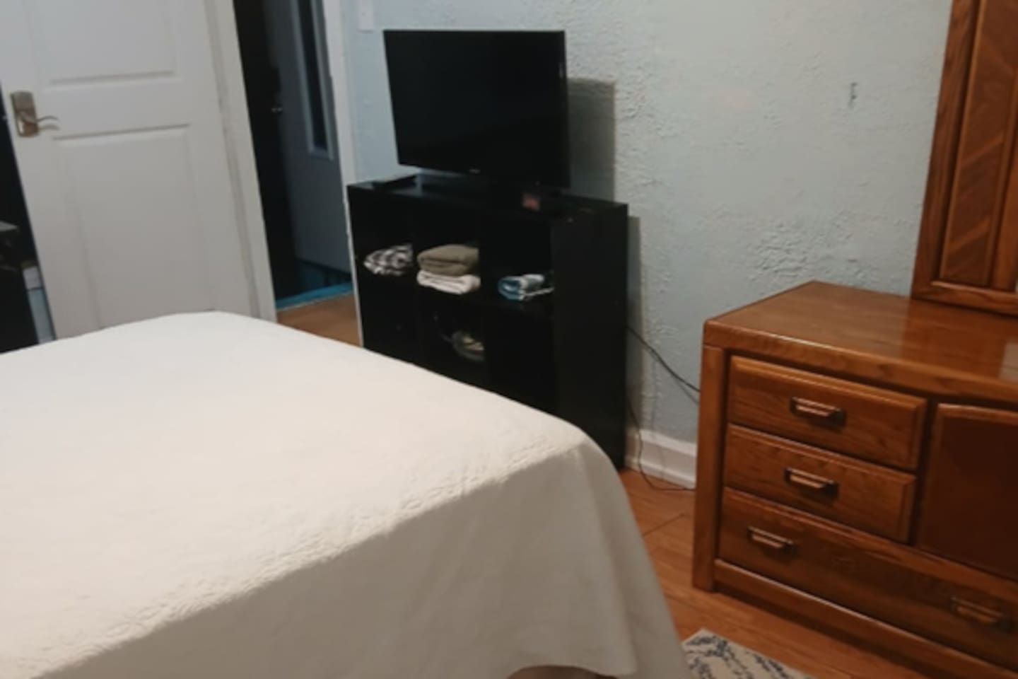 A bedroom with a bed, a wooden dresser, and a television on a stand.