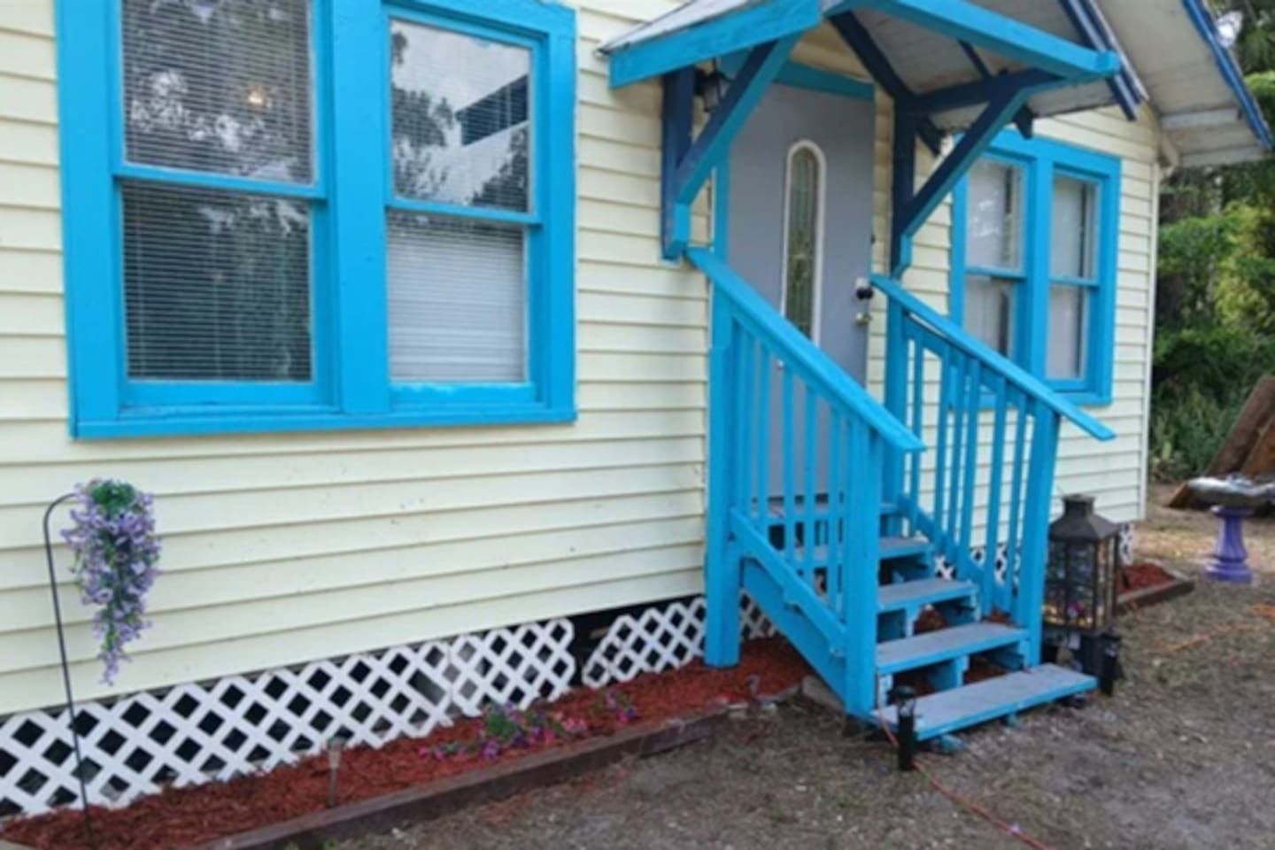 A house with a blue staircase leading to a porch, a white fence, and a small garden area.