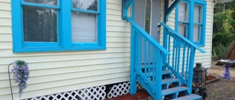 A house with a blue staircase leading to a porch, a white fence, and a small garden area.