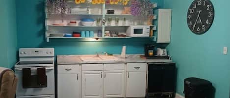 A compact kitchen with white cabinets, a microwave, and a clock on the wall.