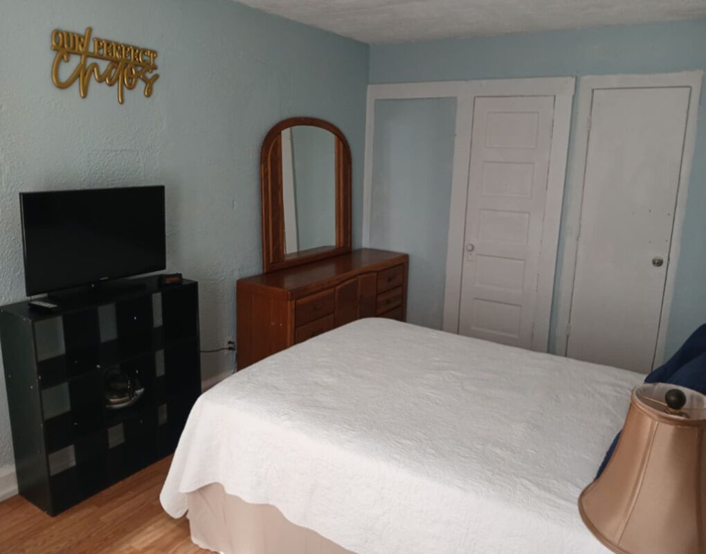 A bedroom with a bed, a dresser, a television, a mirror, and two doors.