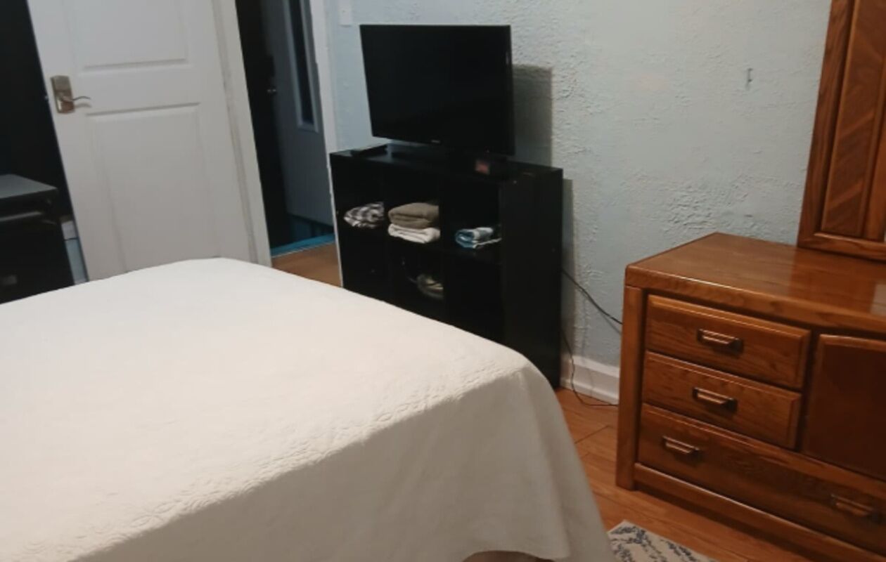 A bedroom with a bed, a wooden dresser, and a television on a stand.