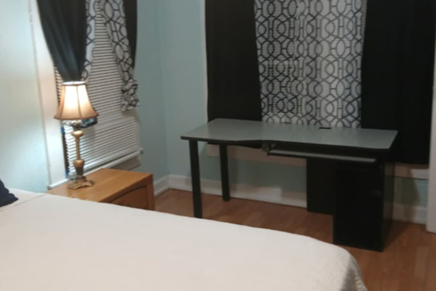 Een kamer met een bed, een klein tafeltje, een bureau en een raam met behang gordijnen.