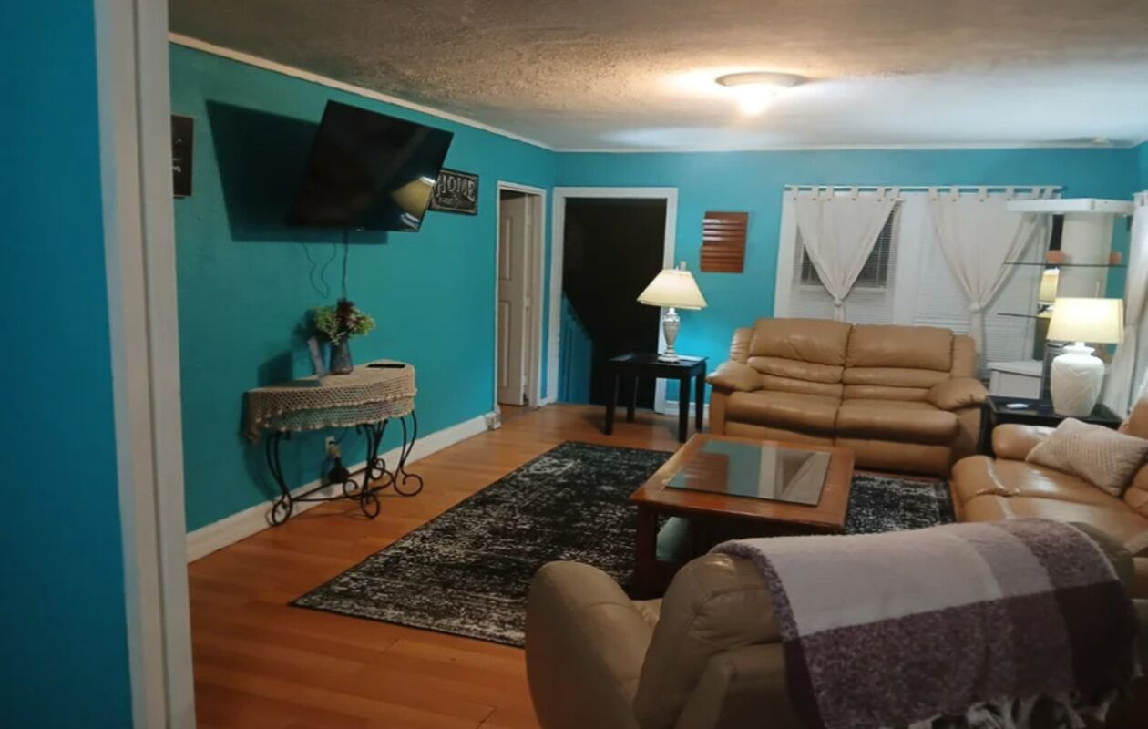 A living room with a sofa, a coffee table, a TV mounted on the wall, and a lamp on a side table.