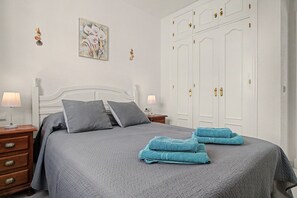 Una cama bien tendida con ropa de cama gris, una mesita de noche con lámpara y un armario grande con varias puertas.