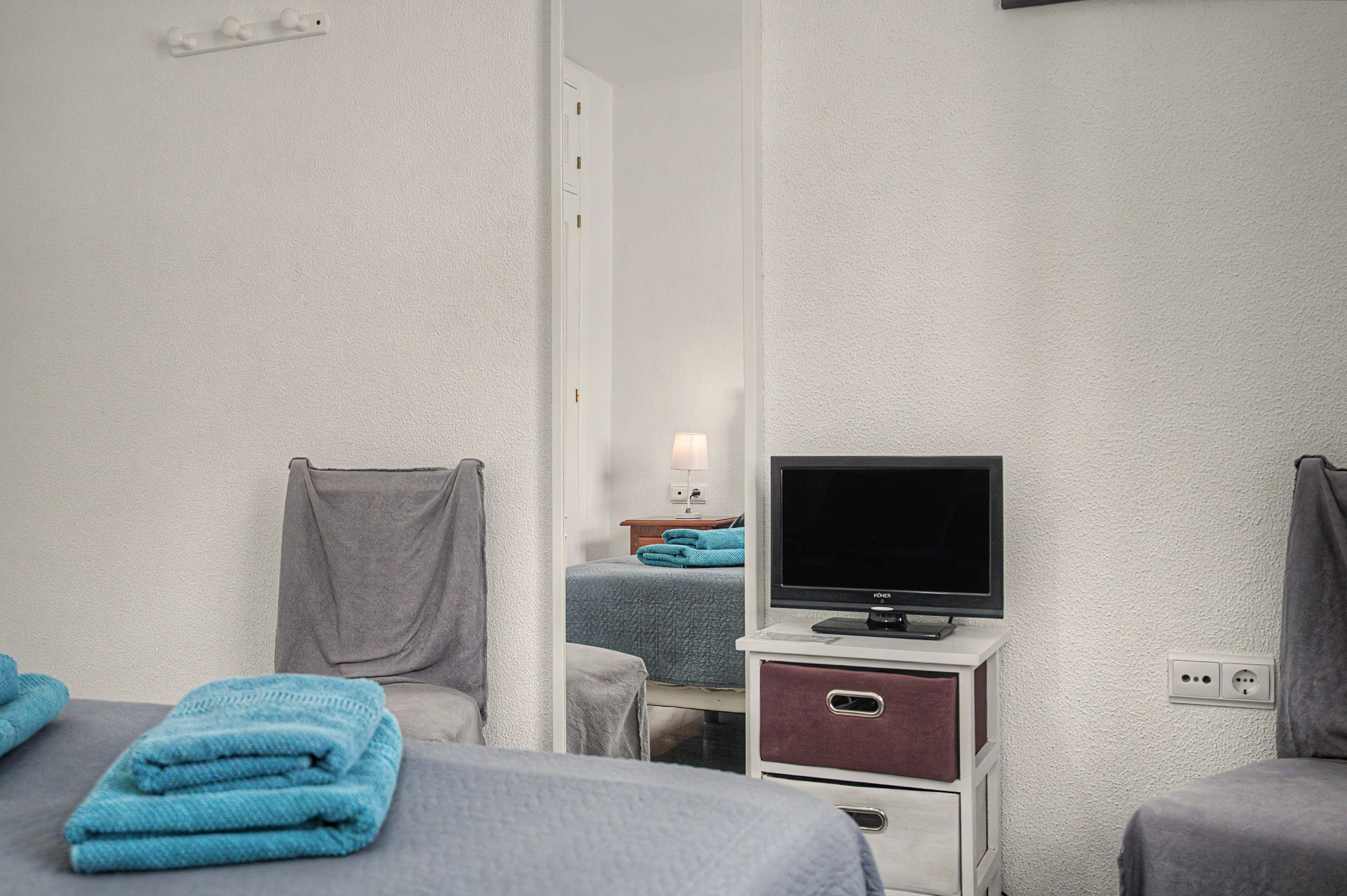Een hotelkamer met twee bedden, een televisie op een standaard, een klein tafeltje met een lamp en een stopcontact.