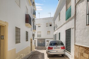 Una calle estrecha con edificios blancos, un coche estacionado y una reja metálica cerrada.