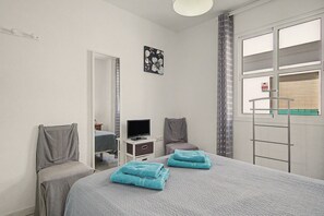 Ein Schlafzimmer mit Bett, Fernseher, Stuhl, Spiegel und einem Fenster mit Blick auf ein Gebäude.