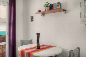 Una mesa redonda con un mantel colorido a rayas, un jarrón decorativo y una estantería en la pared con libros y una planta en maceta.