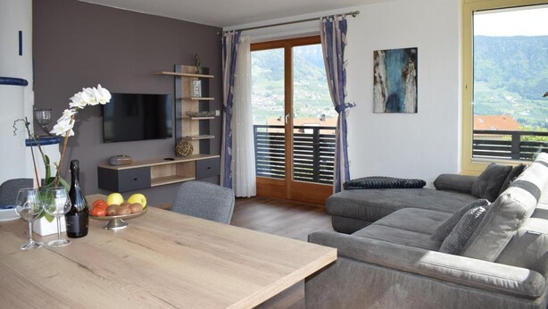 A modern living room with a grey sofa, a wooden dining table, and a TV mounted on the wall. - Apartment 'Residence Ladurn Erde' with Mountain View, Private Terrace and Wi-Fi (Tirol)