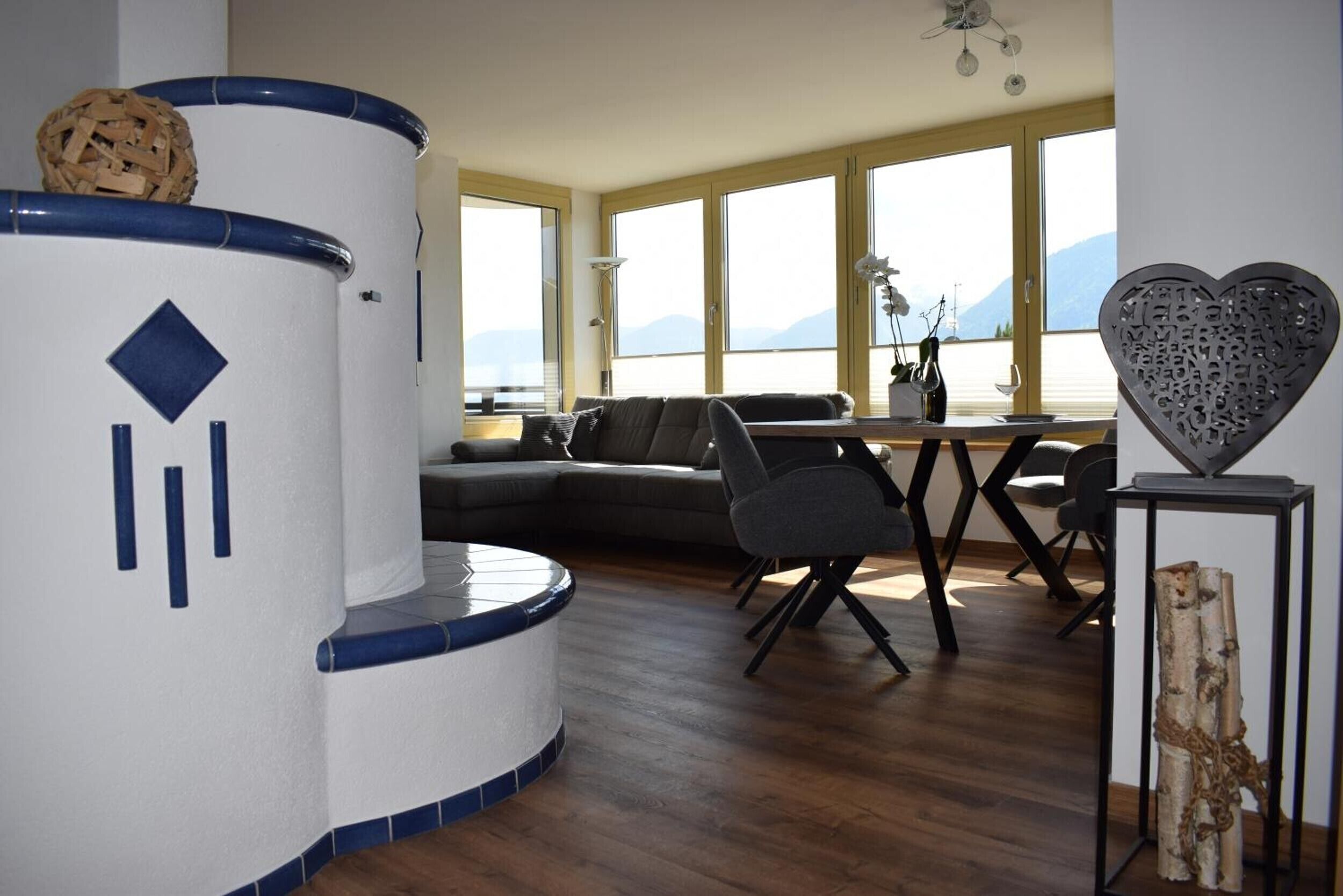 Ein modernes Wohnzimmer mit einer gewölbten weißen und blauen Struktur, einem grauen Sofa und Blick auf Berge durch große Fenster.
