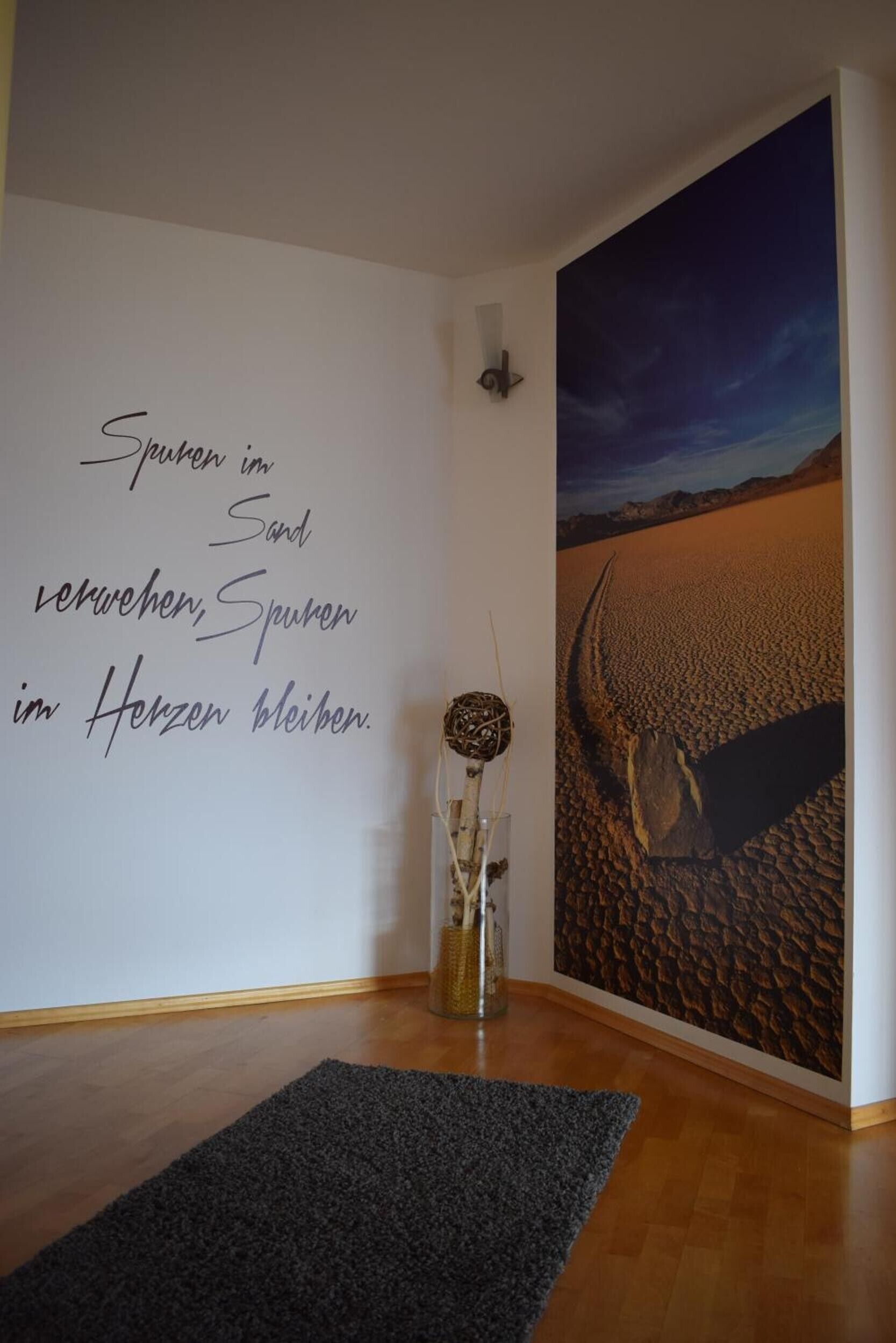 Ein Zimmer mit einer Wand, die eine Wüstenlandschaft zeigt und eine deutsche Schrift trägt.